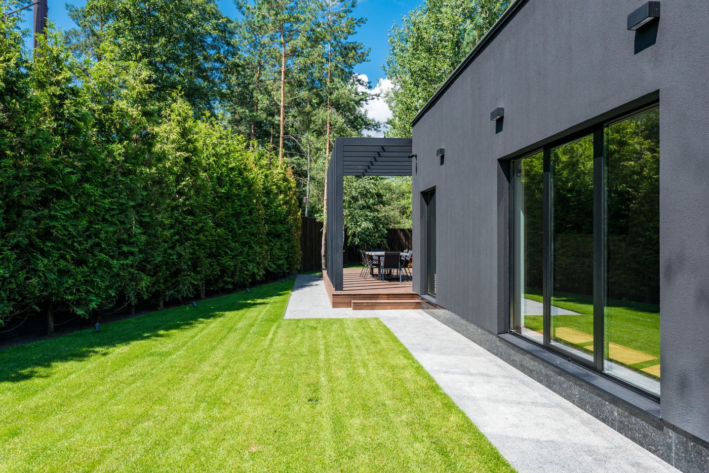 A clean modern backyard with a striped manicured lawn, pergola and trimmed hedges by R&R Landscaping